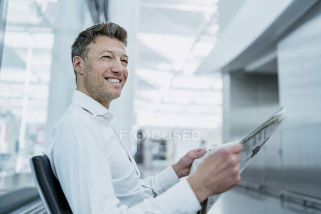 Smiling businessman sitting in waiting area with newspaper — Stock Photo