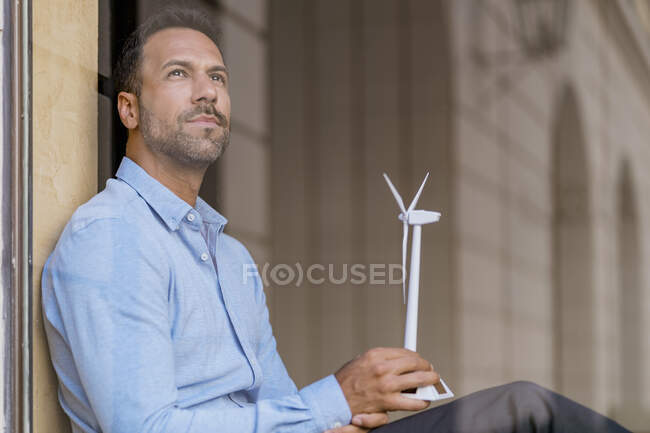 Uomo d'affari con modello di turbina eolica dietro il vetro della finestra pensando — Foto stock
