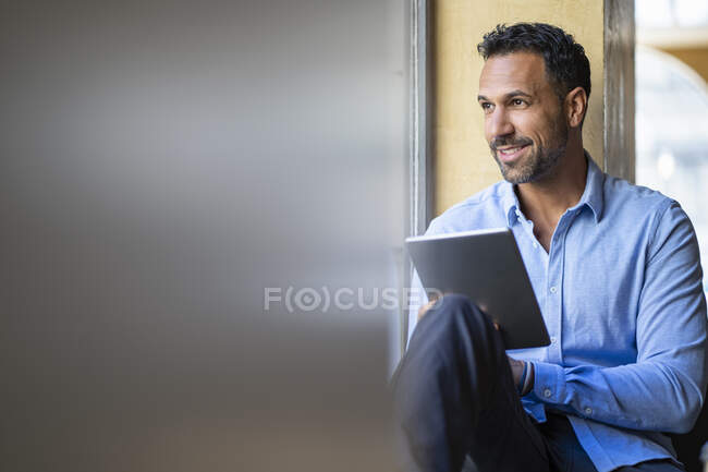 Homme d'affaires souriant assis à la fenêtre en utilisant une tablette — Photo de stock