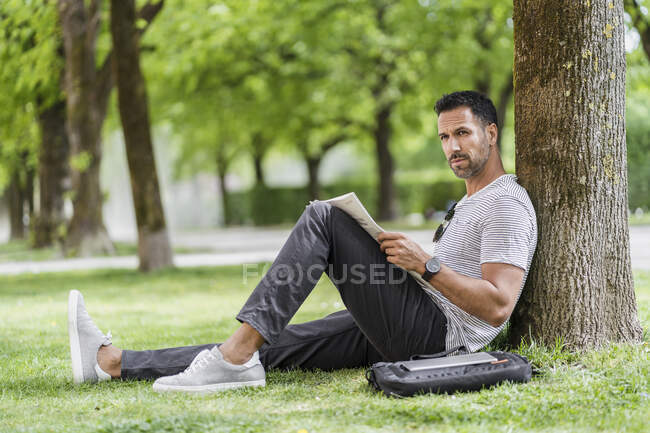 Чоловік спирається на дерево в газеті читання парку — стокове фото