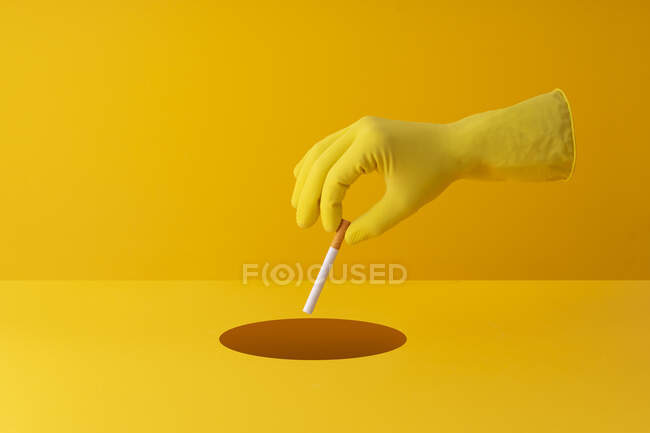 Mão descartar cigarro em um buraco no fundo amarelo — Fotografia de Stock