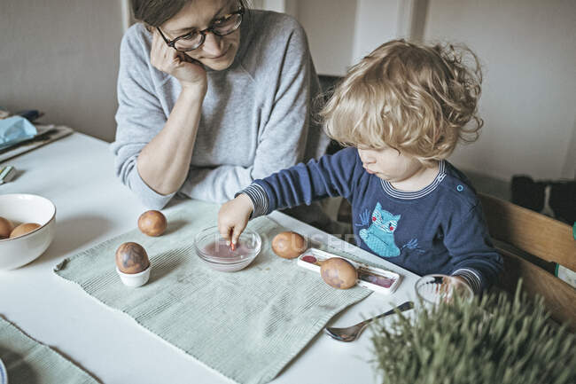 Мати з дочкою сидять за столом і малюють великодні яйця. — стокове фото
