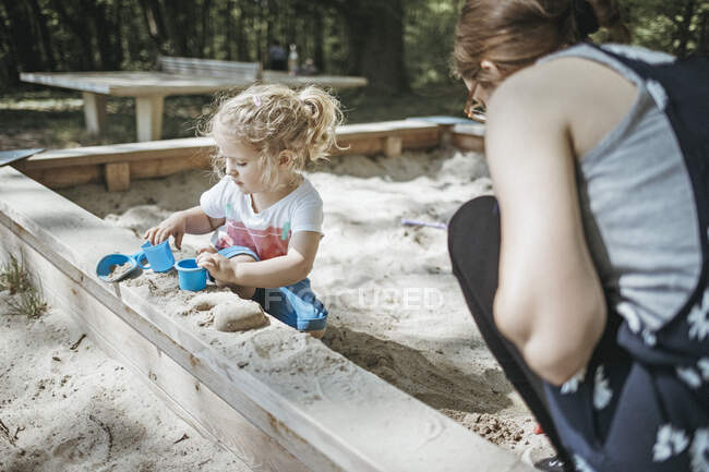 Мама играет с маленькой дочерью в песочнице на детской площадке — стоковое фото