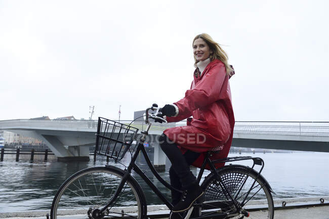 Danemark, Copenhague, femme heureuse en vélo au bord de l'eau par temps pluvieux — Photo de stock