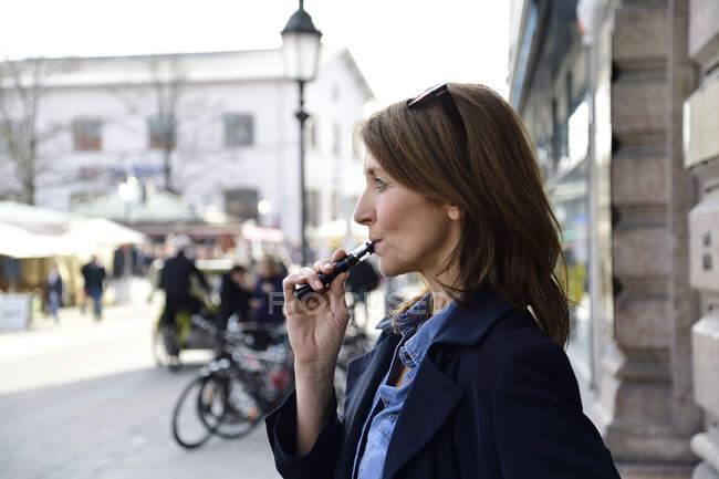 Mujer madura fumando cigarrillo electrónico en la ciudad - foto de stock