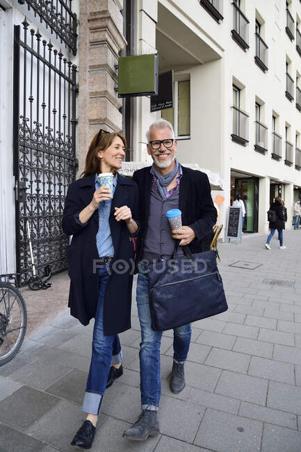 Couple mature souriant avec tasses en bambou réutilisables marchant dans la ville — Photo de stock