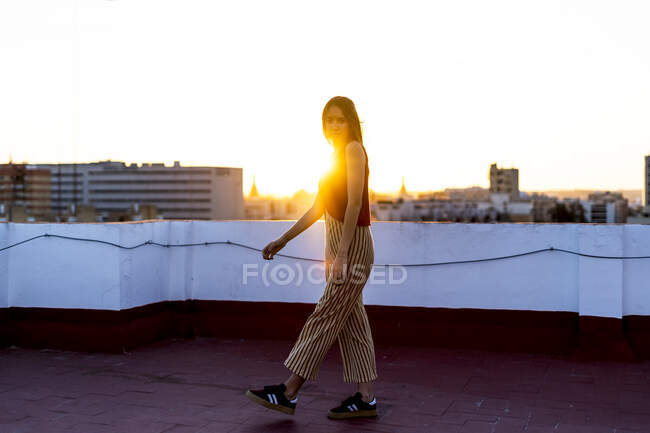 Дівчина-підліток, що йде на терасі на даху в місті на заході сонця — стокове фото
