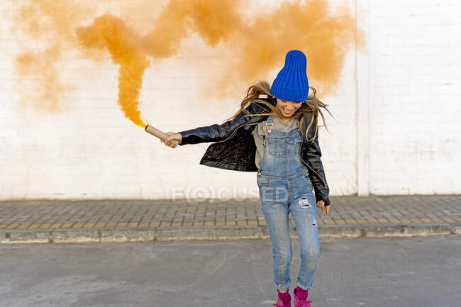 Fille souriante avec torche de fumée orange dans la rue — Photo de stock