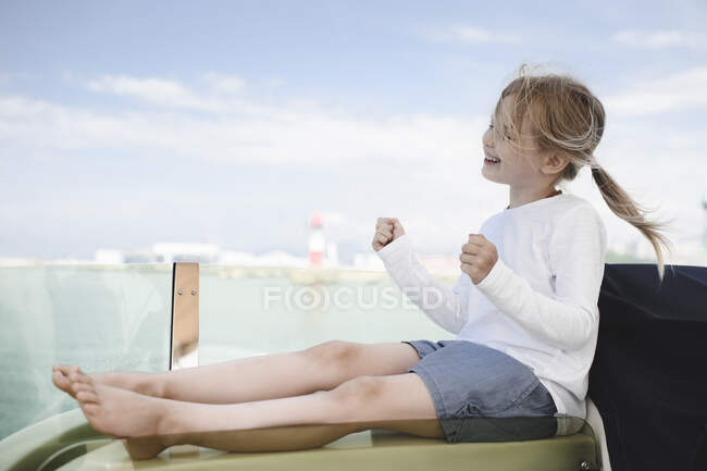 Happy little girl sitting on lounger clenching fists — Stock Photo