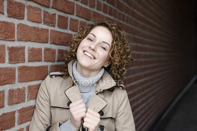 Portrait of smiling woman with curly hair wearing trenchcoat and turtleneck pullover — Stock Photo