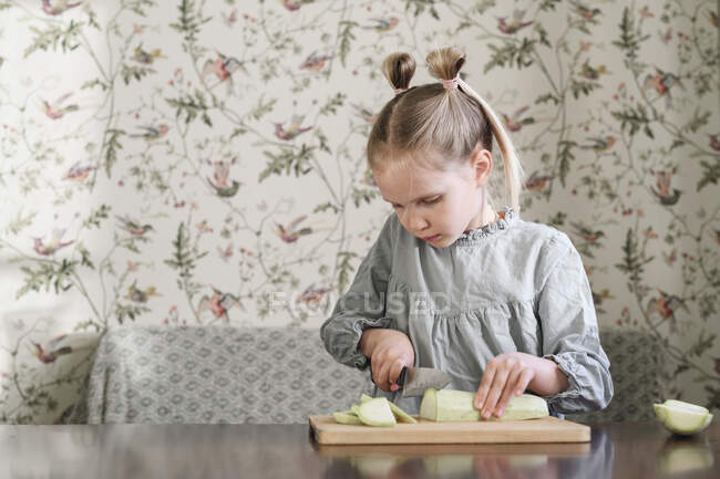Girl slicing courgette indoors — Stock Photo