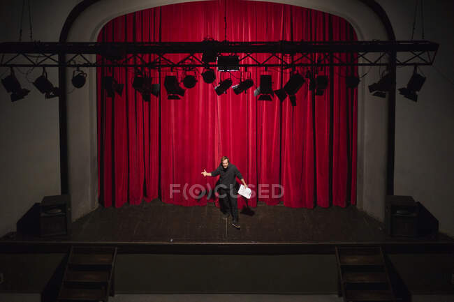 Репетиція актора з сценарієм, що стоїть на театральній сцені перед червоною завісою — стокове фото