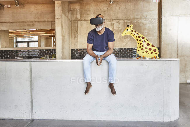 Зрілий бізнесмен в сучасному офісі, сидячи поруч з фігурою жирафа в окулярах VR — стокове фото