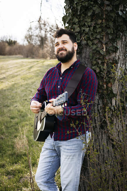 Mann spielt Gitarre an einem Baum auf einer Wiese — Stockfoto