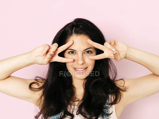 Portrait of young smiling woman with black hair and hands on face, in front of pink background — Stock Photo