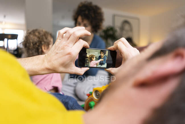 Mère et fille jouant dans le salon, fater prendre des photos smartphone — Photo de stock