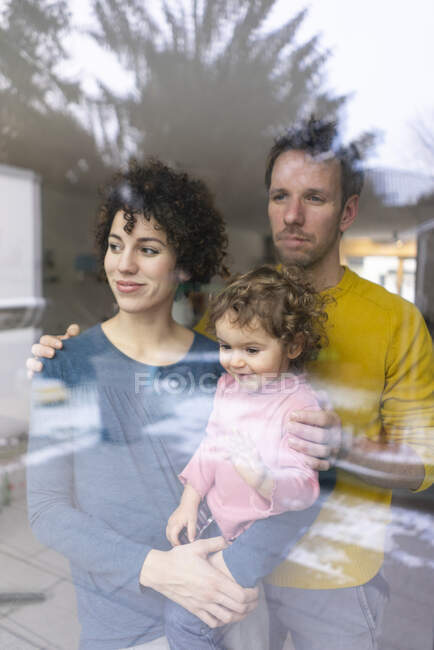 Happy family looking out of window, mother carrying daughter — Stock Photo