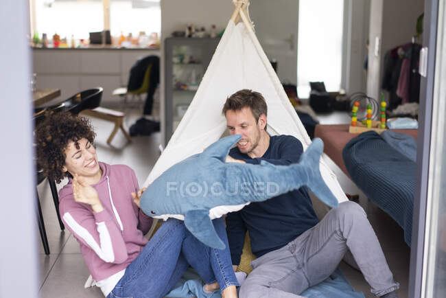 Пара драк с игрушечной акулой, сидящей в гостиной, перед игровой палаткой — стоковое фото