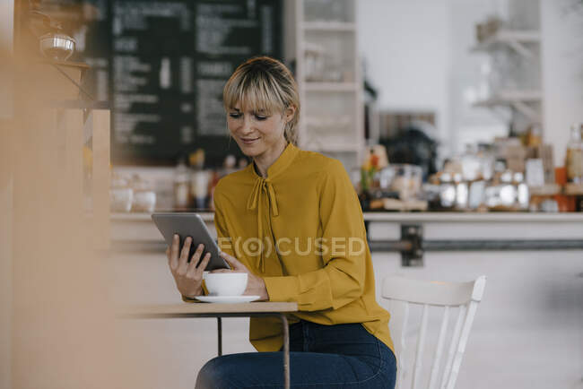 Donna d'affari bionda che usa lo smartphone in una caffetteria, legge messaggi di testo — Foto stock