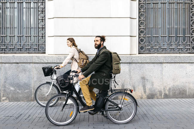 Пара їздить на електронному велосипеді в місті, проходить повз будинок. — стокове фото