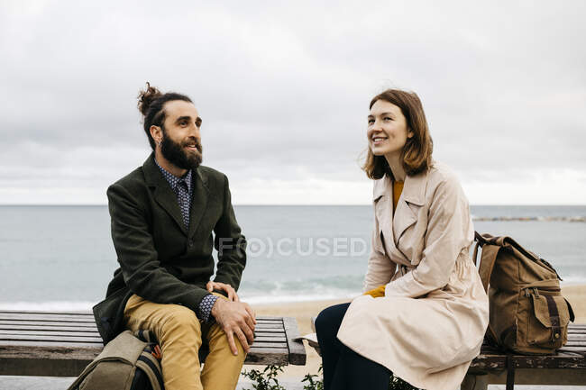 Lächelndes Paar sitzt auf einer Bank an der Strandpromenade und redet — Stockfoto