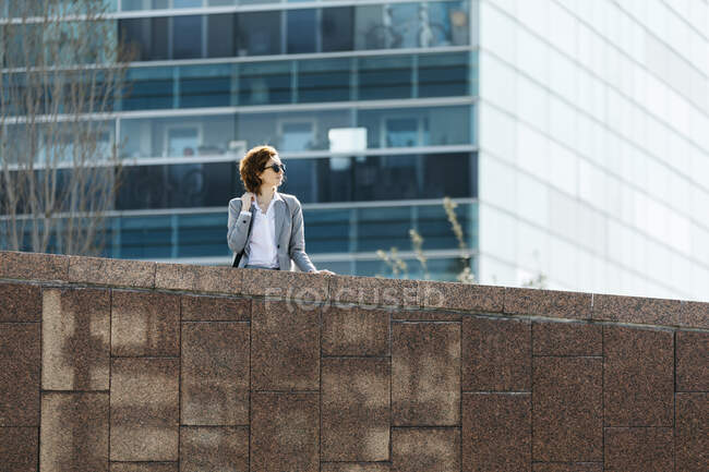 Joven empresaria exitosa parada en la pared frente al edificio de oficinas - foto de stock