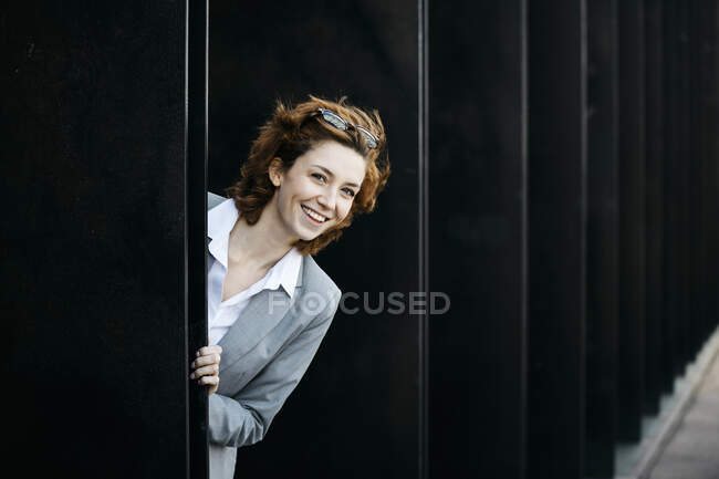 Glückliche junge Geschäftsfrau guckt aus Fassade eines Bürogebäudes — Stockfoto