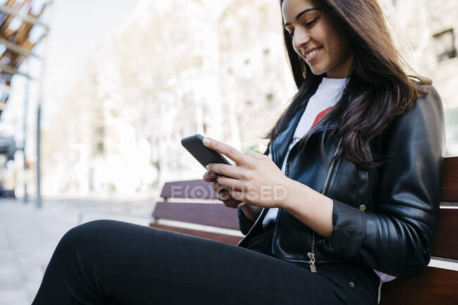 Молодая женщина сидит на скамейке, используя смартфон — стоковое фото