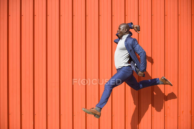 Empresario saltando en el aire frente a la pared naranja - foto de stock
