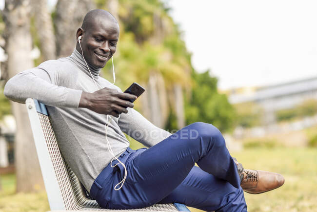 Портрет усміхненого бізнесмена, який сидить на лавці слухає музику з навушниками та смартфонами — стокове фото