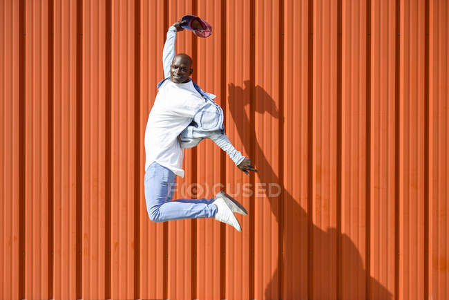 Man wearing casual denim clothes jumping in the air in front of orange wall — Stock Photo