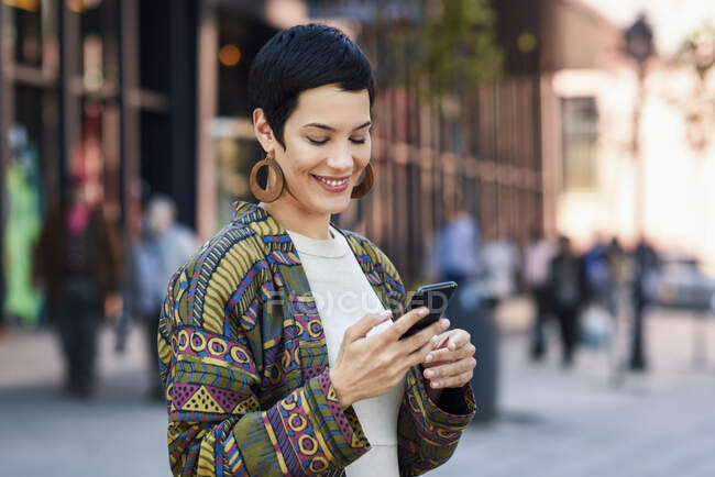 Усміхнена модна молода жінка використовує мобільний телефон у місті — стокове фото