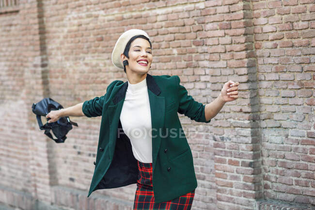Happy fashionable young woman wearing a beret and a green jacket at a brick wall — Stock Photo