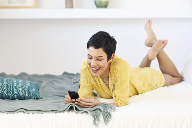 Щаслива молода жінка використовує мобільний телефон у ліжку — стокове фото
