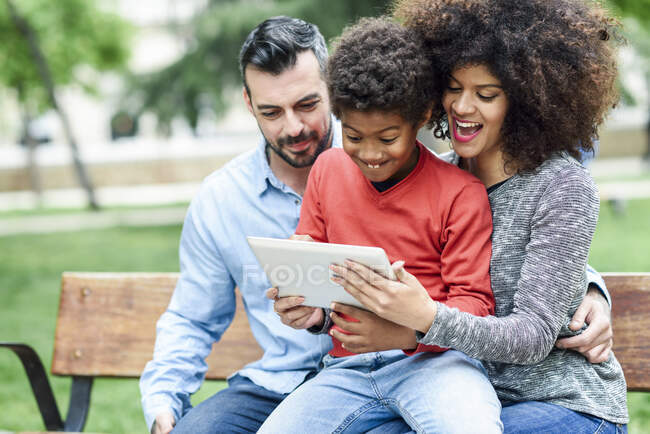 Родина сидить на лавці в парку, користуючись цифровим планшетом. — стокове фото