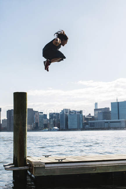 USA, New York, Brooklyn, giovane che fa il salto del Parkour dal palo di legno davanti allo skyline di Manhattan — Foto stock