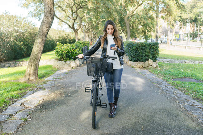 Молодая женщина с велосипедом в парке с помощью мобильного телефона — стоковое фото