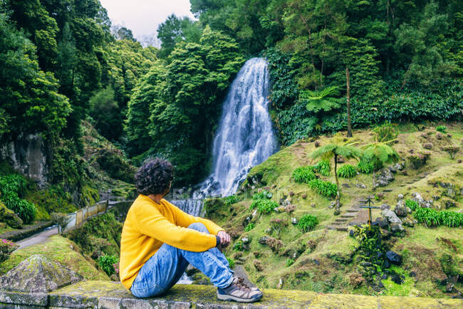 Portugal, Islas Azores, Sao Miguel, sentado mirando una cascada - foto de stock