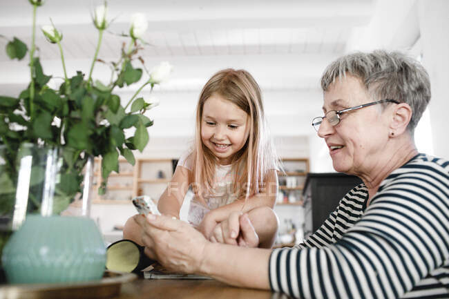 Happy grandmother with cell phone and granddaughter at home — Stock Photo