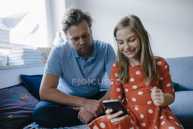 Padre e hija usando el teléfono celular en casa - foto de stock