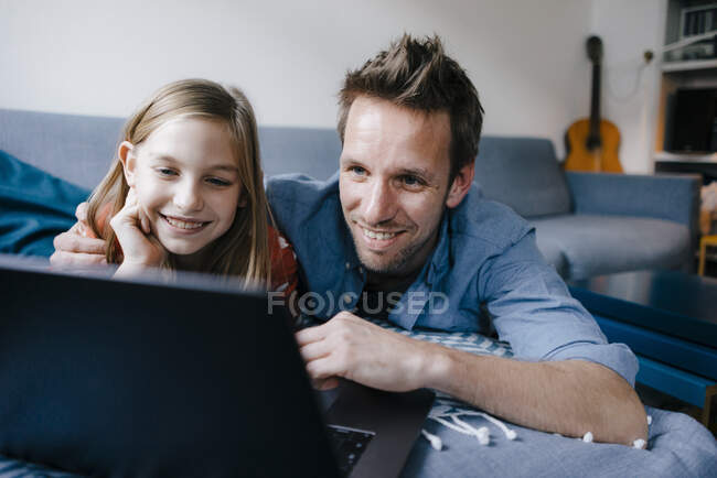 Père et fille heureux couchés sur le canapé à la maison en utilisant un ordinateur portable — Photo de stock