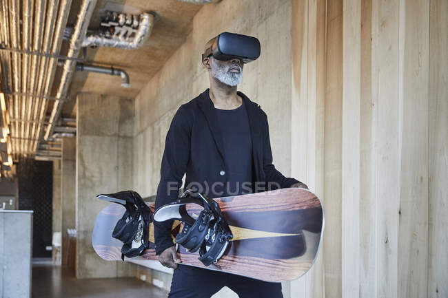 Mature businessman wearing VR glasses holding snowboard in modern office — Stock Photo