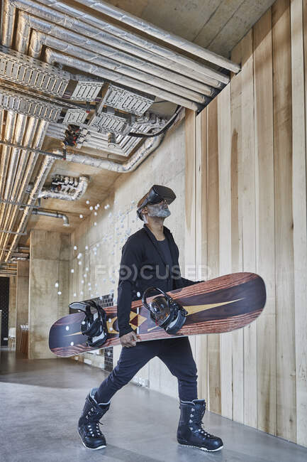 Зрелый бизнесмен в очках VR держит сноуборд в современном офисе — стоковое фото