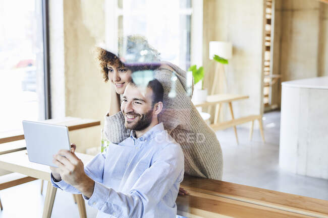 Улыбающийся мужчина и женщина делятся планшетом в современном офисе — стоковое фото