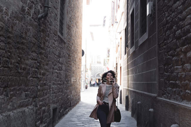 Femme heureuse parlant sur un téléphone portable dans une ruelle — Photo de stock