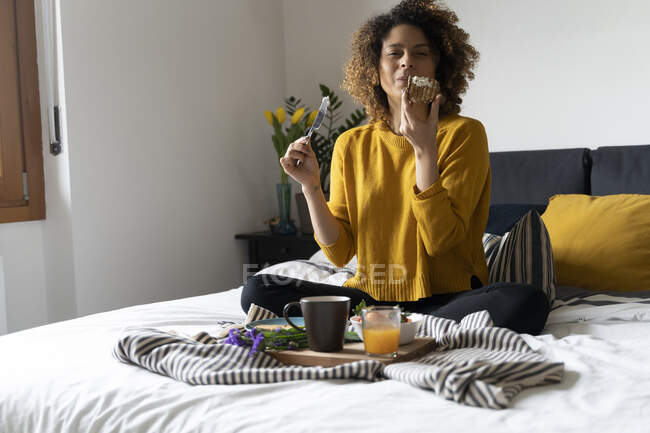 Mujer sentada en la cama, desayunando sano - foto de stock
