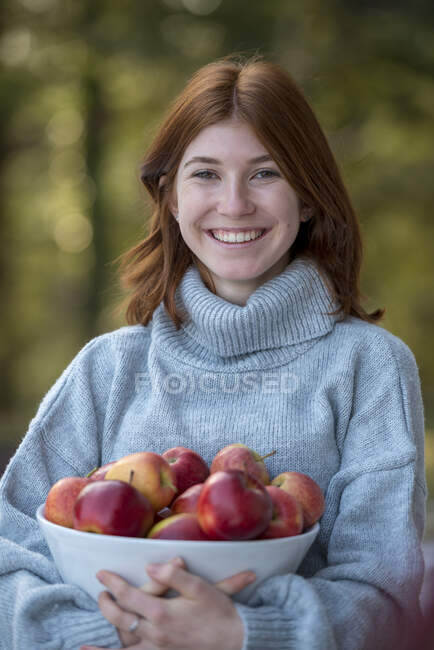 Portrait of happy redheaded teenage girl holding bowl of apples — Stock Photo