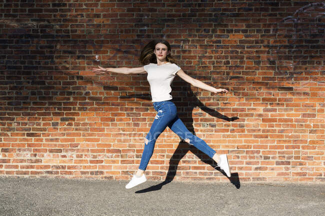 Mujer joven ágil saltando frente a la pared de ladrillo — Stock Photo