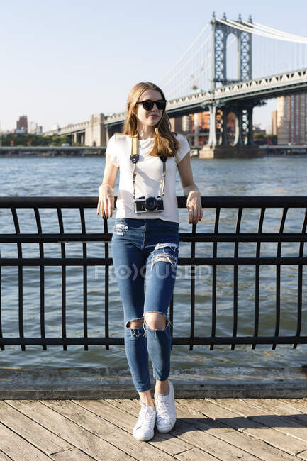 Giovane donna che esplora New York, in piedi al ponte di Brooklyn con la macchina fotografica — Foto stock