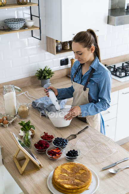 Young woman preparing a cream cake, using tablet — Stock Photo
